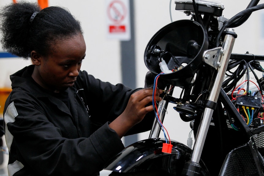 A woman works on a partially assembled motorcycle in a industrial setting