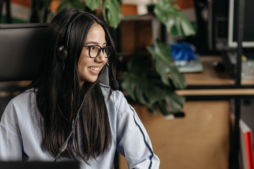 A girl in glasses and a headset smiles at someone off camera.
