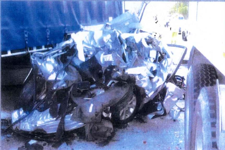 A grainy photo of a crashed car next to a truck with a blue cover.