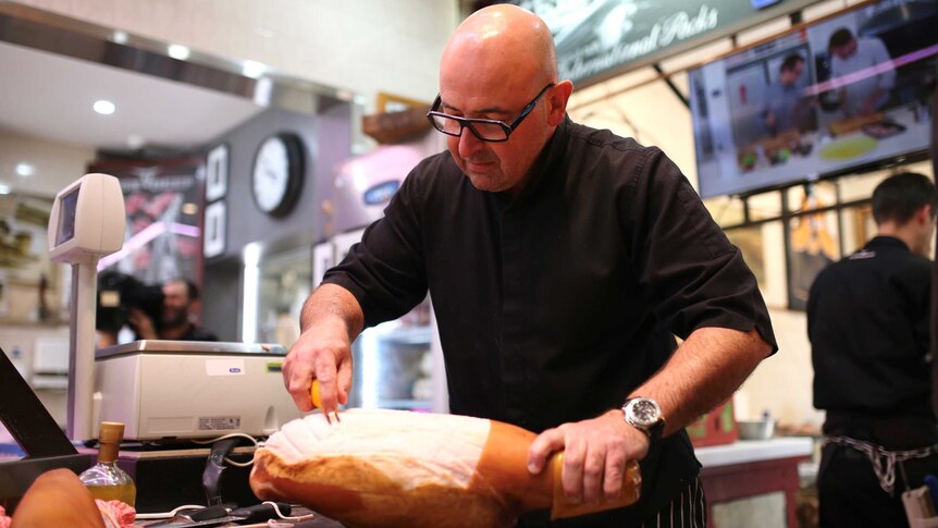 A butcher scores a ham inside his shop.