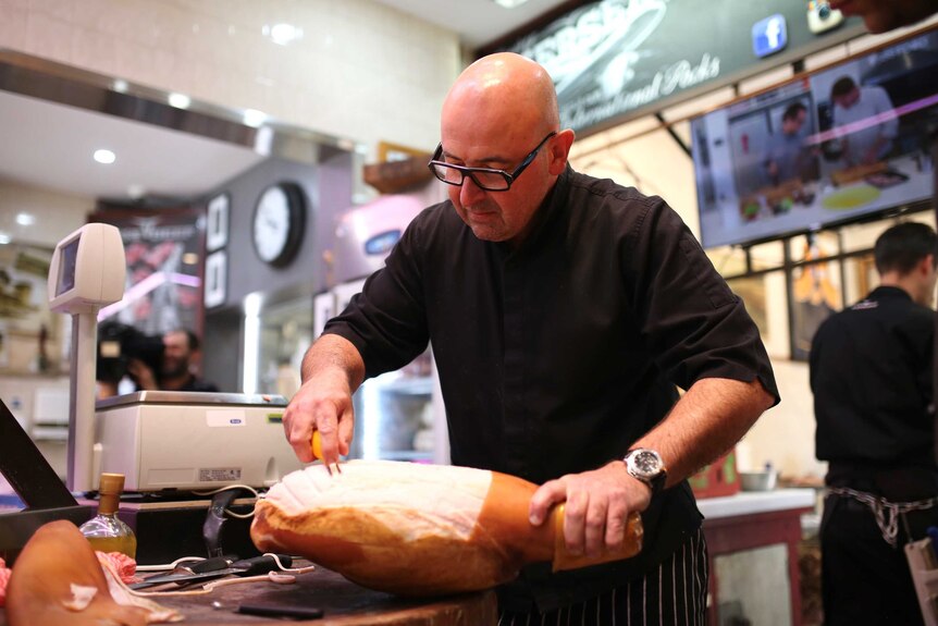 A butcher scores a ham inside his shop.