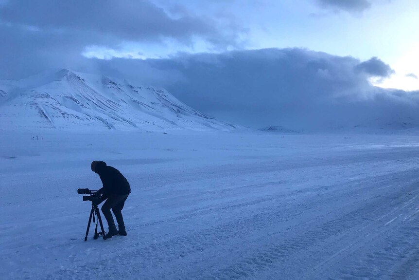 Stephen Schubert with camera in silhouette against white Artic landscape.