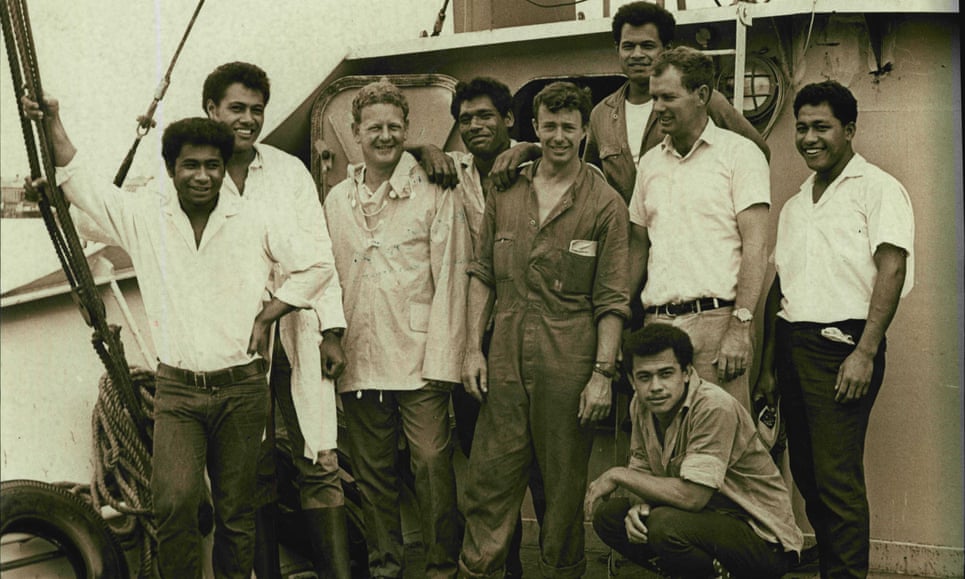 A Caucasian man stands with Tongan men on a boat.