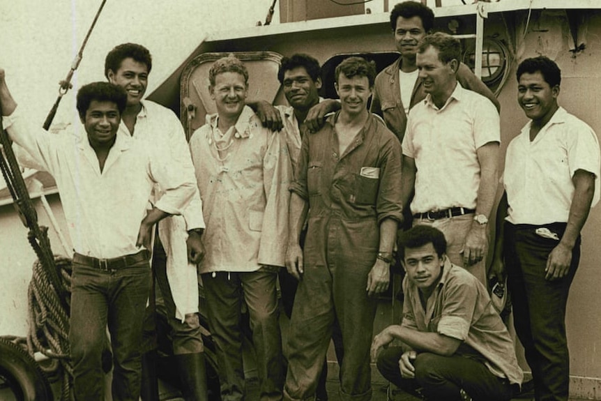 A Caucasian man stands with Tongan men on a boat.