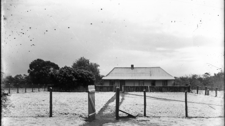 An old black and white photo of a farmstead in the snow.