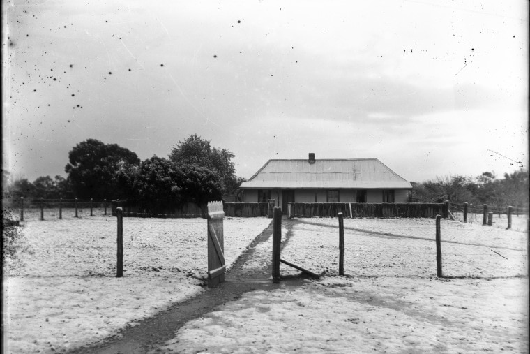 An old black and white photo of a farmstead in the snow.