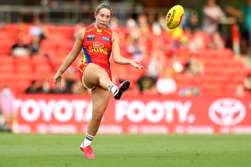 AFLW player Jacqui Yorston, in a Gold Coast pride guernsey, kicks the ball