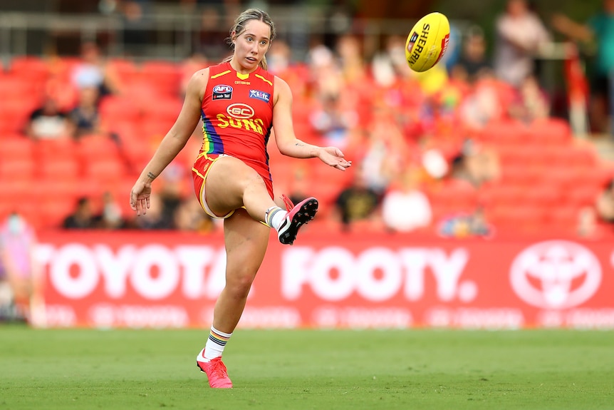 AFLW player Jacqui Yorston, in a Gold Coast pride guernsey, kicks the ball
