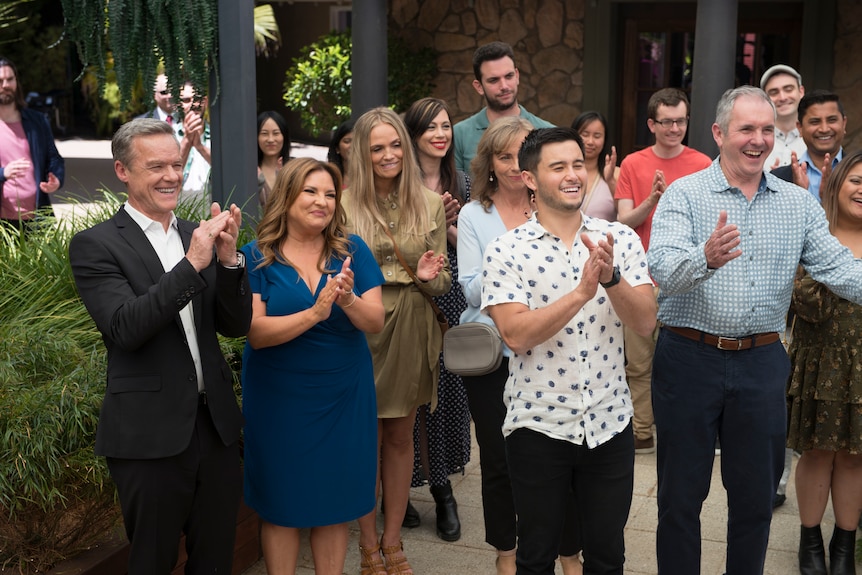 A group of people clapping and smiling, looking just to the right of the camera.