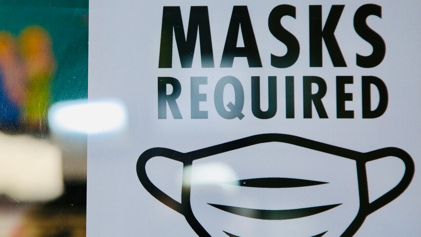 A white sign with black text reads 'MASKS REQUIRED' with an image of a mask.