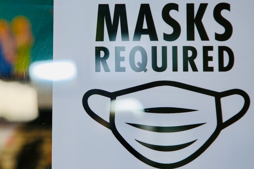 A white sign with black text reads 'MASKS REQUIRED' with an image of a mask.