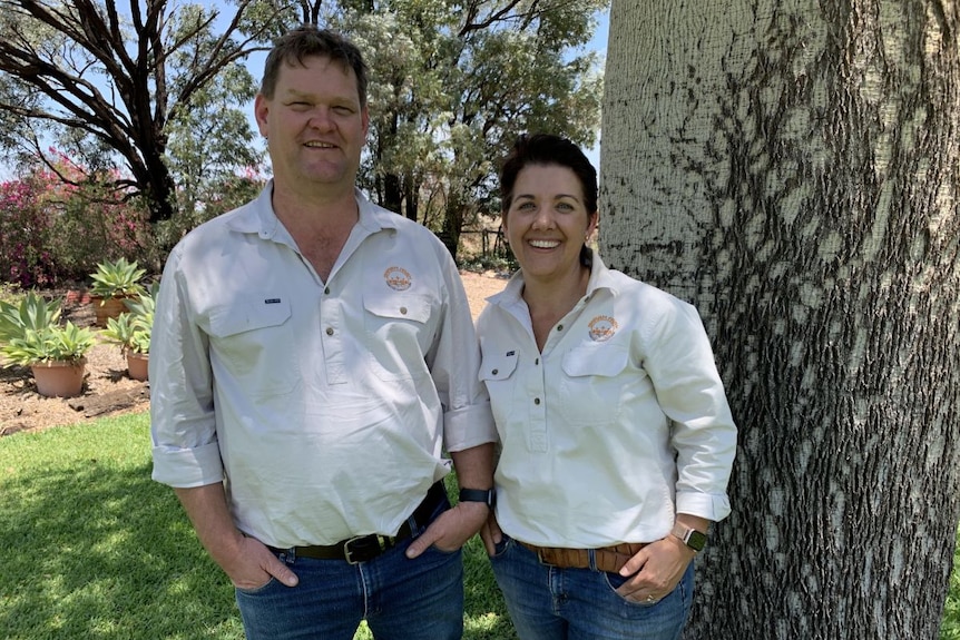 A man and woman in beige shirts and jeans smile at the camera.