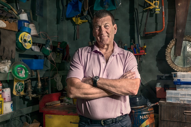 A man stands in a shed surrounded by tools.