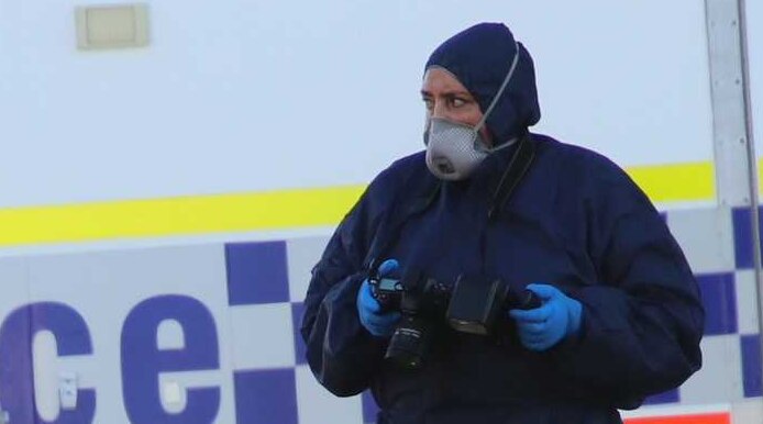 A forensic police officer holds a camera in front of a police van.