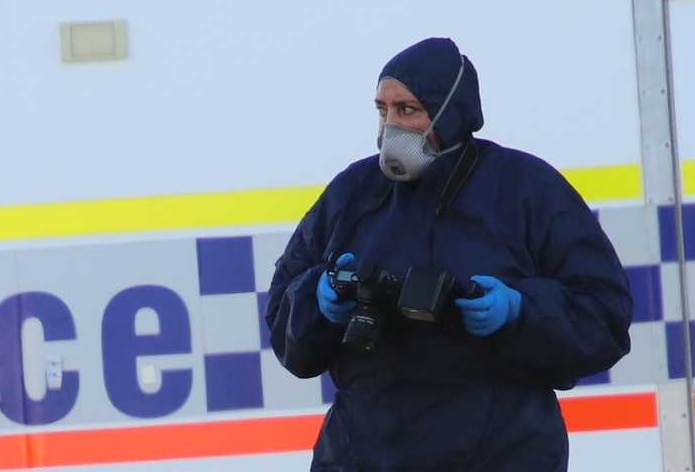A forensic police officer holds a camera in front of a police van.