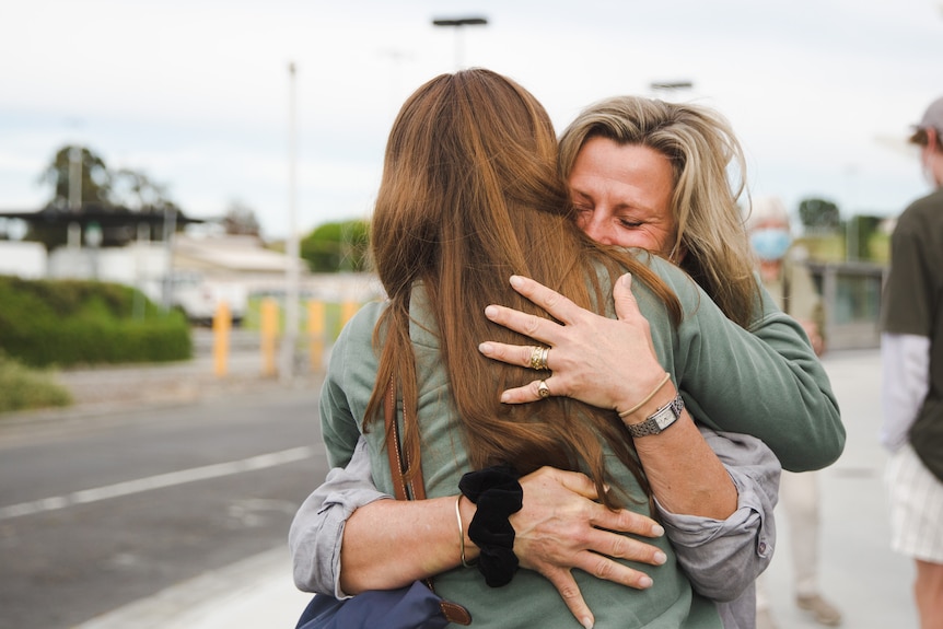 A middle aged woman hugs a younger woman with long brown hair