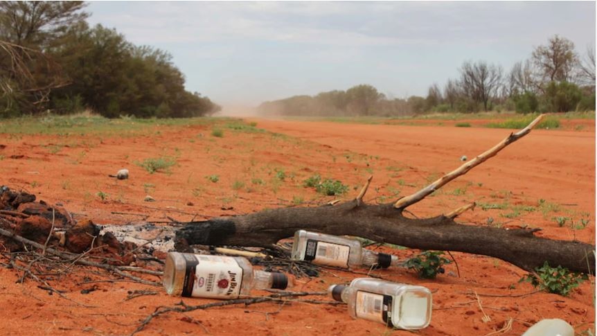 Empty alcohol bottles lay by a roadside of red dirt.
