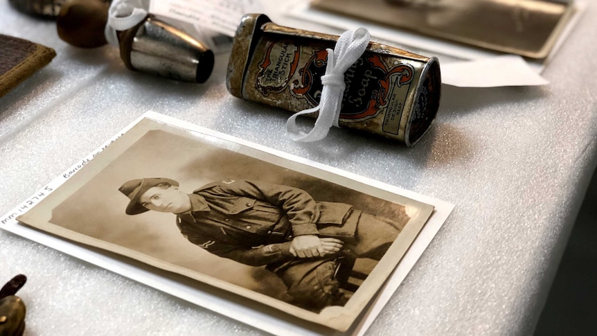 Old photographs and a battered tin are laid out on a table.