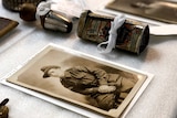 Old photographs and a battered tin are laid out on a table.