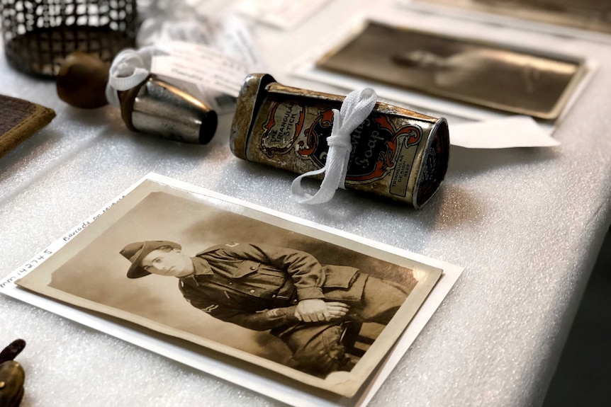 Old photographs and a battered tin are laid out on a table.