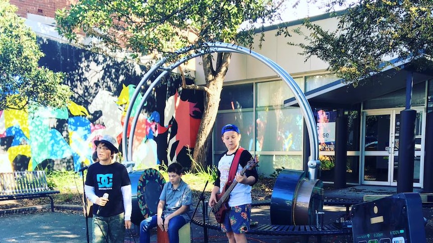 A set of giant headphones on a street, with teenagers  playing music and busking on the street.