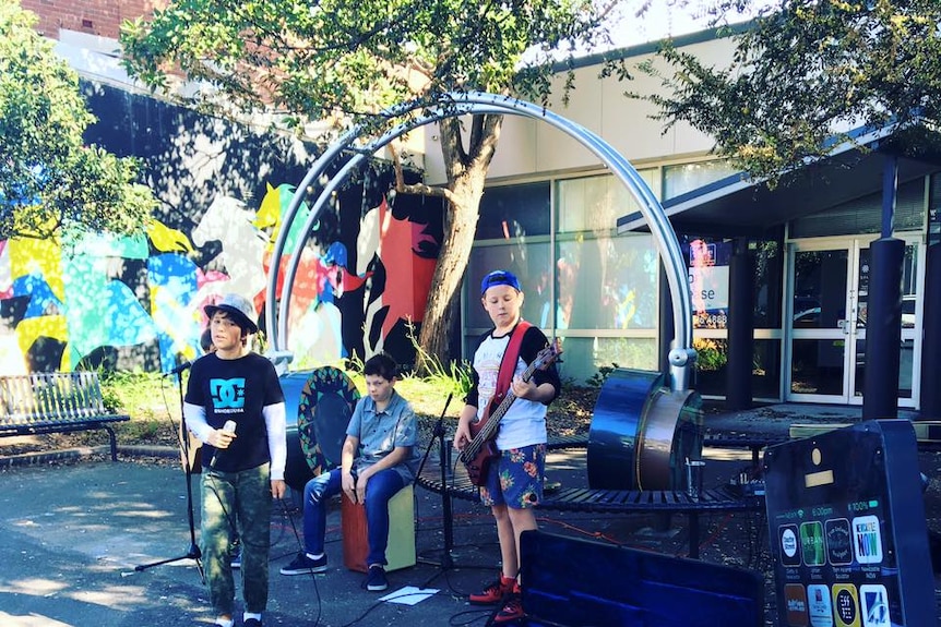 A set of giant headphones on a street, with teenagers  playing music and busking on the street.