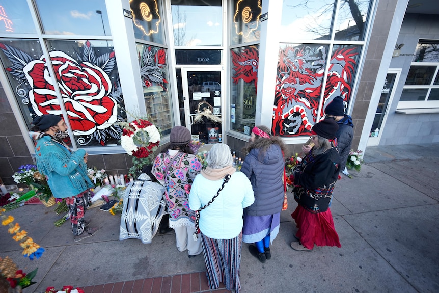 Mourners gather outside the door of a tattoo parlor. 
