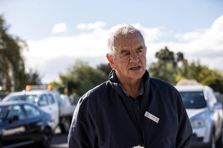 A man with a blue jumper and grey hair looks off to the side.