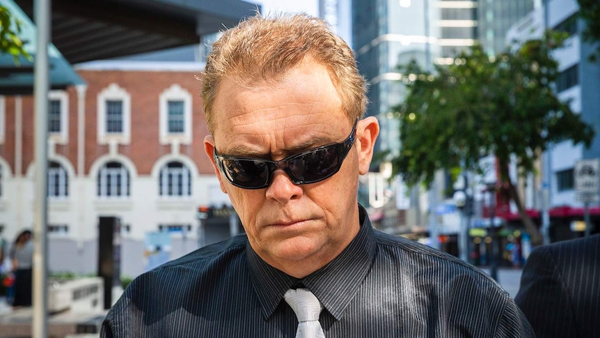 Police officer Neil Punchard, wearing sunglasses, walks down street outside the Magistrates Court in Brisbane.