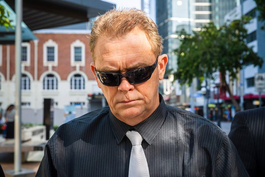 Police officer Neil Punchard, wearing sunglasses, walks down street outside the Magistrates Court in Brisbane.