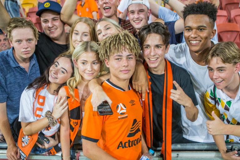 A young footballer with dreadlocks smiles for a photo with young fans.