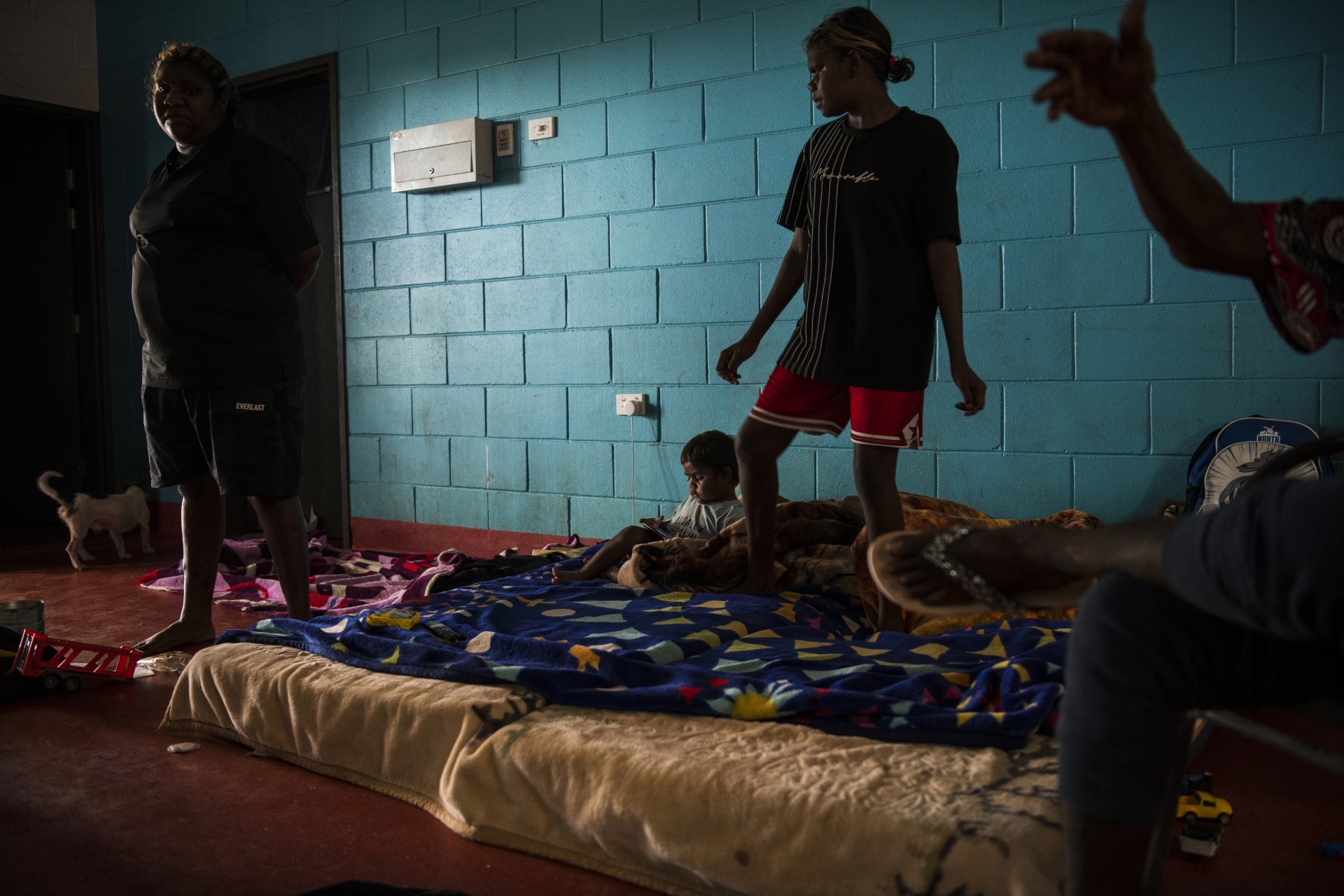 The interior of a house with blue concrete walls and a mattress on a floor with people standing next to it