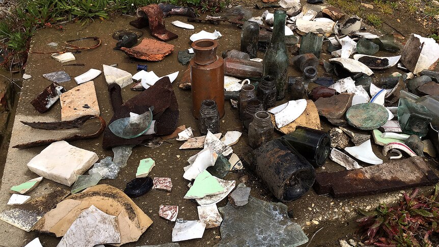 Old bottles, vases and tiles pictured on a slab of concrete.