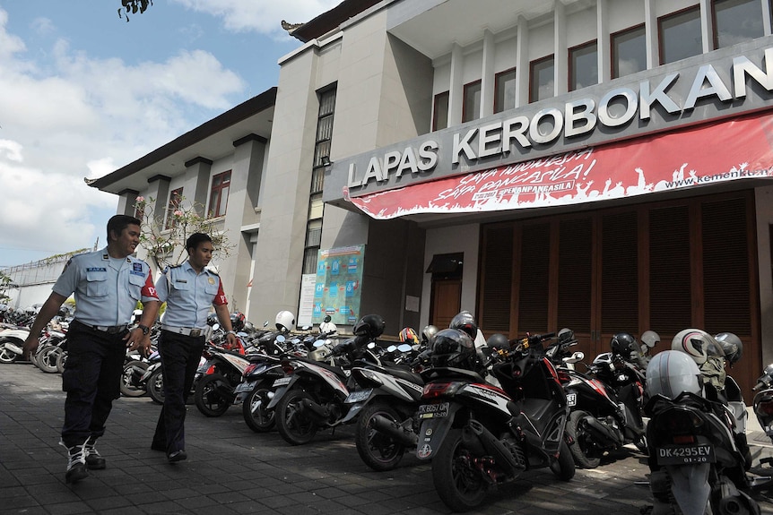 Two security guards walk past a line of motorbikes outside Bali's Kerobokan prison.