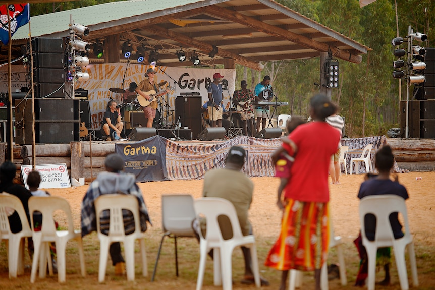 A band performing on a stage with a poster that says "garma" at the front of the stage.