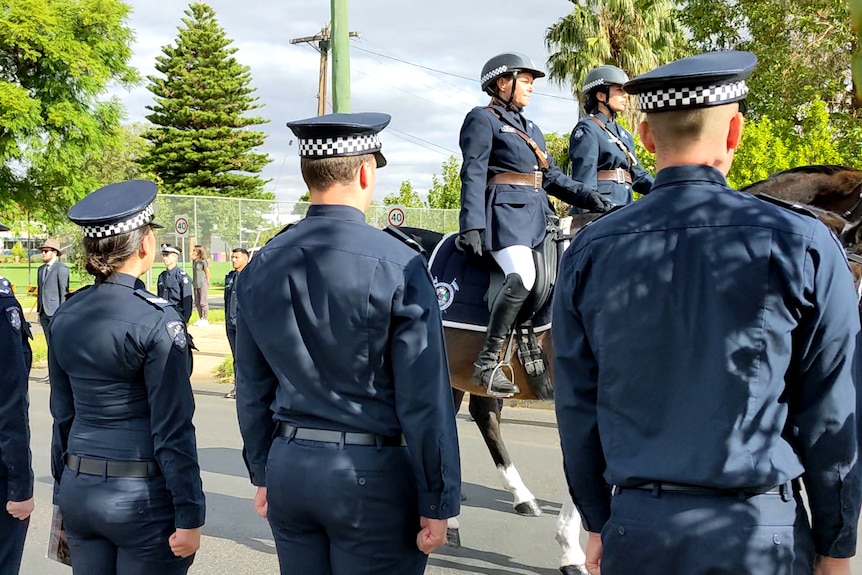 Scores of police form a guard of honour along a street at the funeral of a colleague.