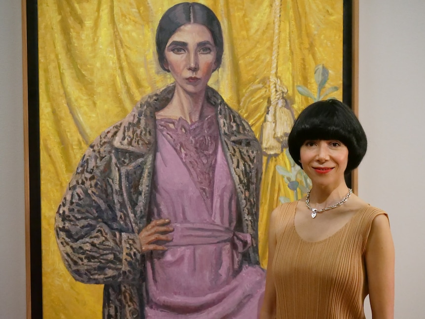 A woman poses in front of a self-portrait at the National Portrait Gallery in Canberra