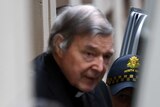 Cardinal George Pell is led into a van while being escorted by police.
