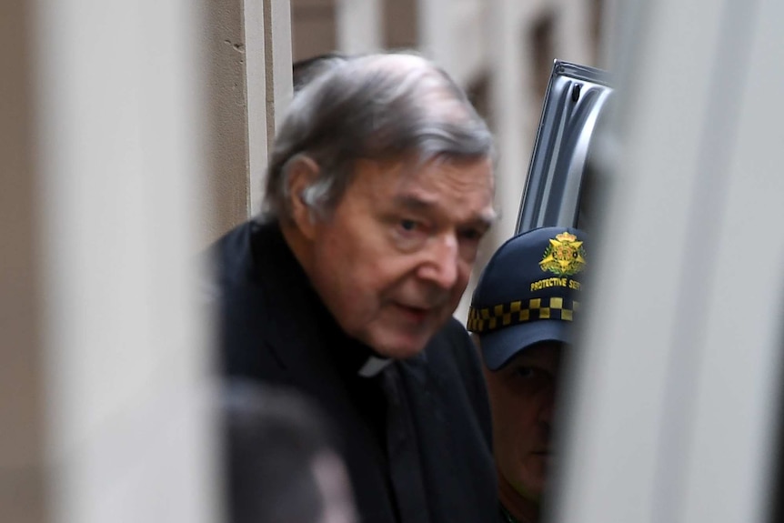 Cardinal George Pell is led into a van while being escorted by police.