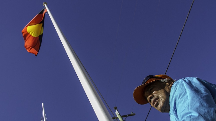 An Indigenous man raises the Aboriginal and Torres Strait Island flags.