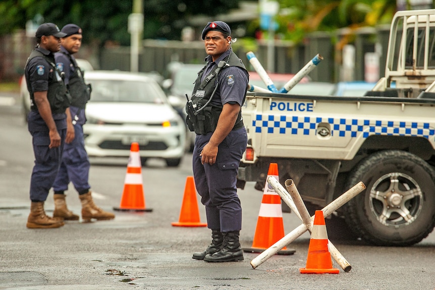 A police man standing on road in front of orange cones and police vehicle