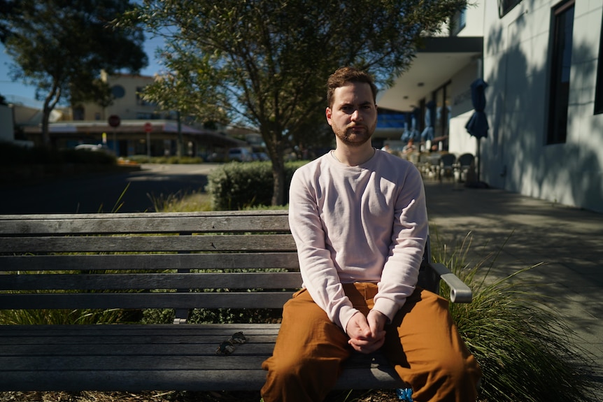 Zac Morris sits on a park bench. He has a stern look on his face.