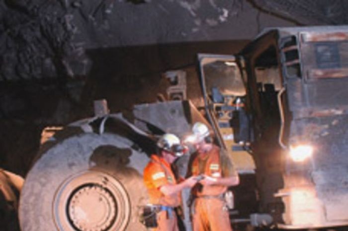 Two underground coal miners stands beside a vehicle in a mine shaft at a mine in Australia.
