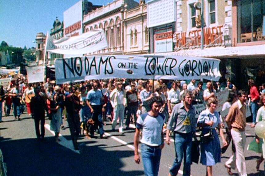 A grainy photograph of protesters walking through a Launceston street holding a banner that says, "No dams on the lower Gordon"