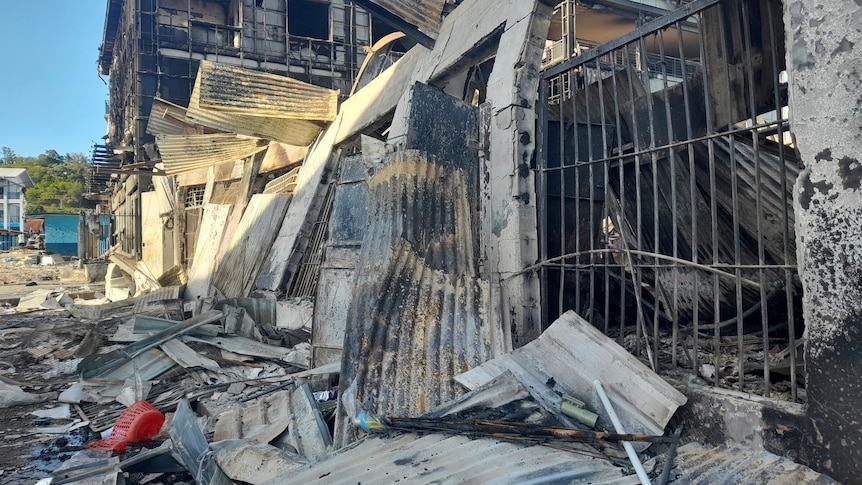 Burned and destroyed buildings line a street overrun by looters with wreckage scattered across the ground.