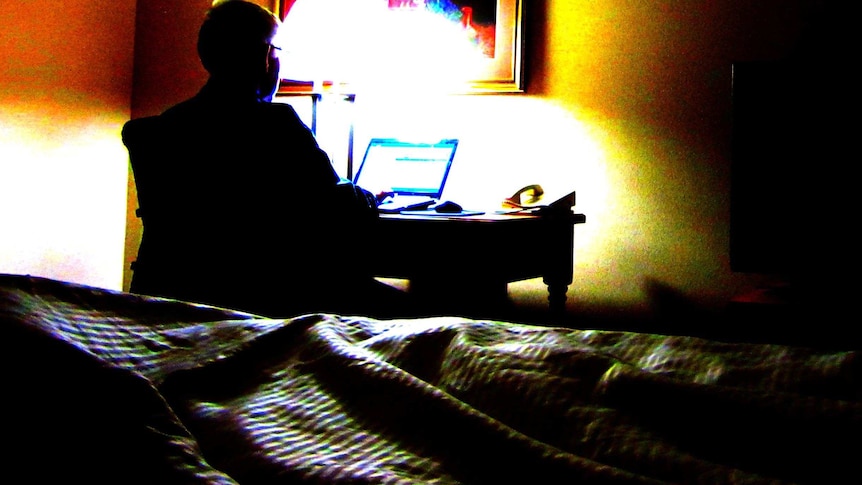 A man sits at a laptop computer in a dark room.