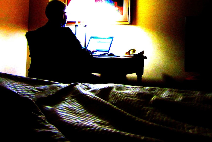 A man sits at a laptop computer in a dark room.