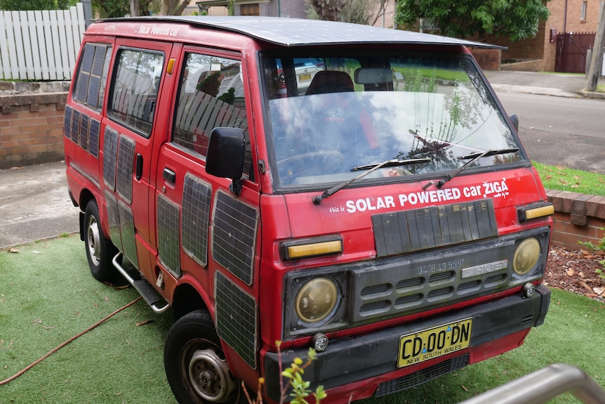 A red van covered in solar panels parked in a front yard