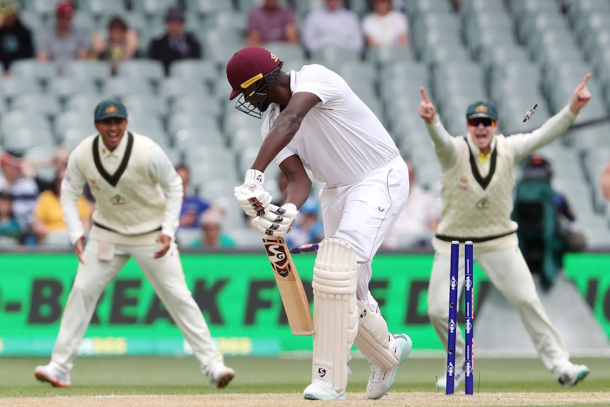 The Australian slip cordon throw their arms up in triumph as the bails fly and a West Indian batsman is bowled.