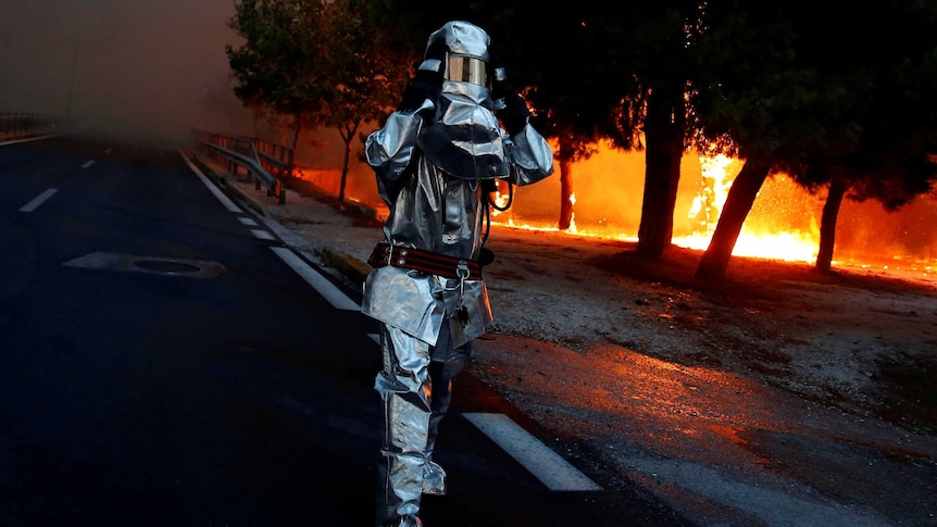 A firefighter wears a flame resistant uniform as wildfire burns in the town of Rafina.
